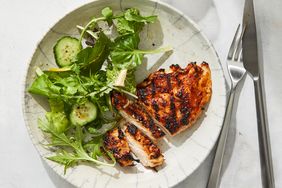 A plate with sliced grilled chicken and a mixed green salad with cucumber slices