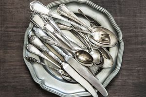 A stack of various utensils including spoons forks and knives on a plate