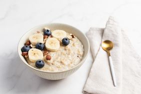 Bowl of oatmeal topped with banana slices blueberries and chopped nuts next to a spoon and napkin on a table