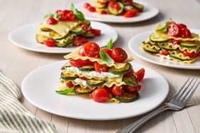 Layered dishes featuring slices of vegetables pasta sheets and ricotta cheese on white plates garnished with fresh ingredients