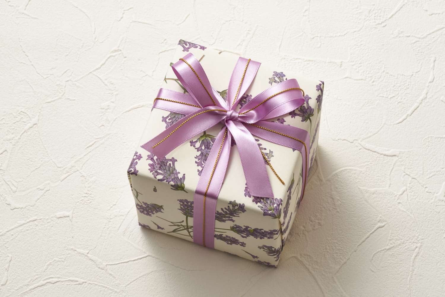 A gift box wrapped in decorative floral paper with a satin ribbon bow on top