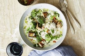 A bowl of rice topped with broccoli tofu cubes and a curry sauce served with garnishes