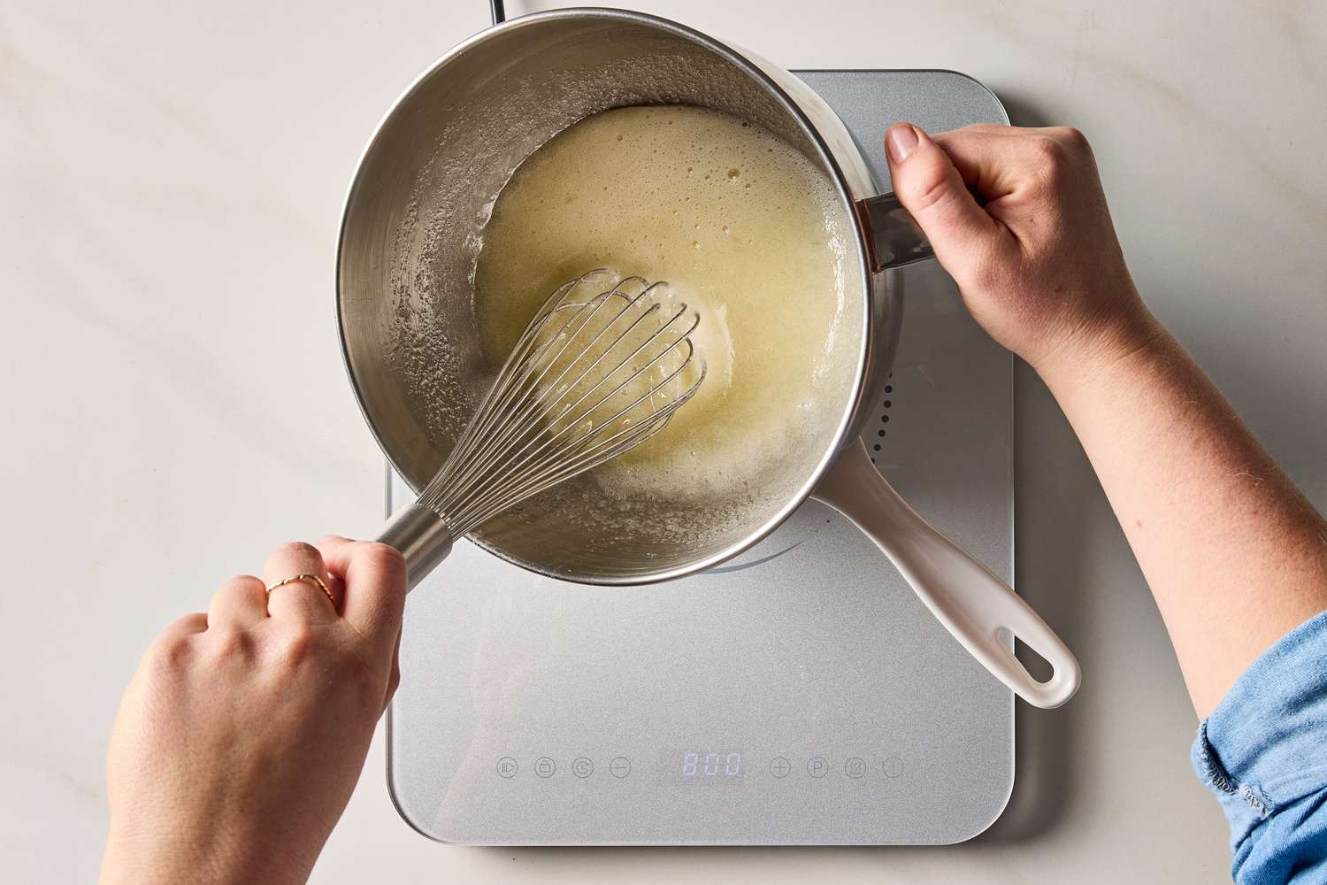 Hands whisking a mixture in a saucepan over an induction cooktop