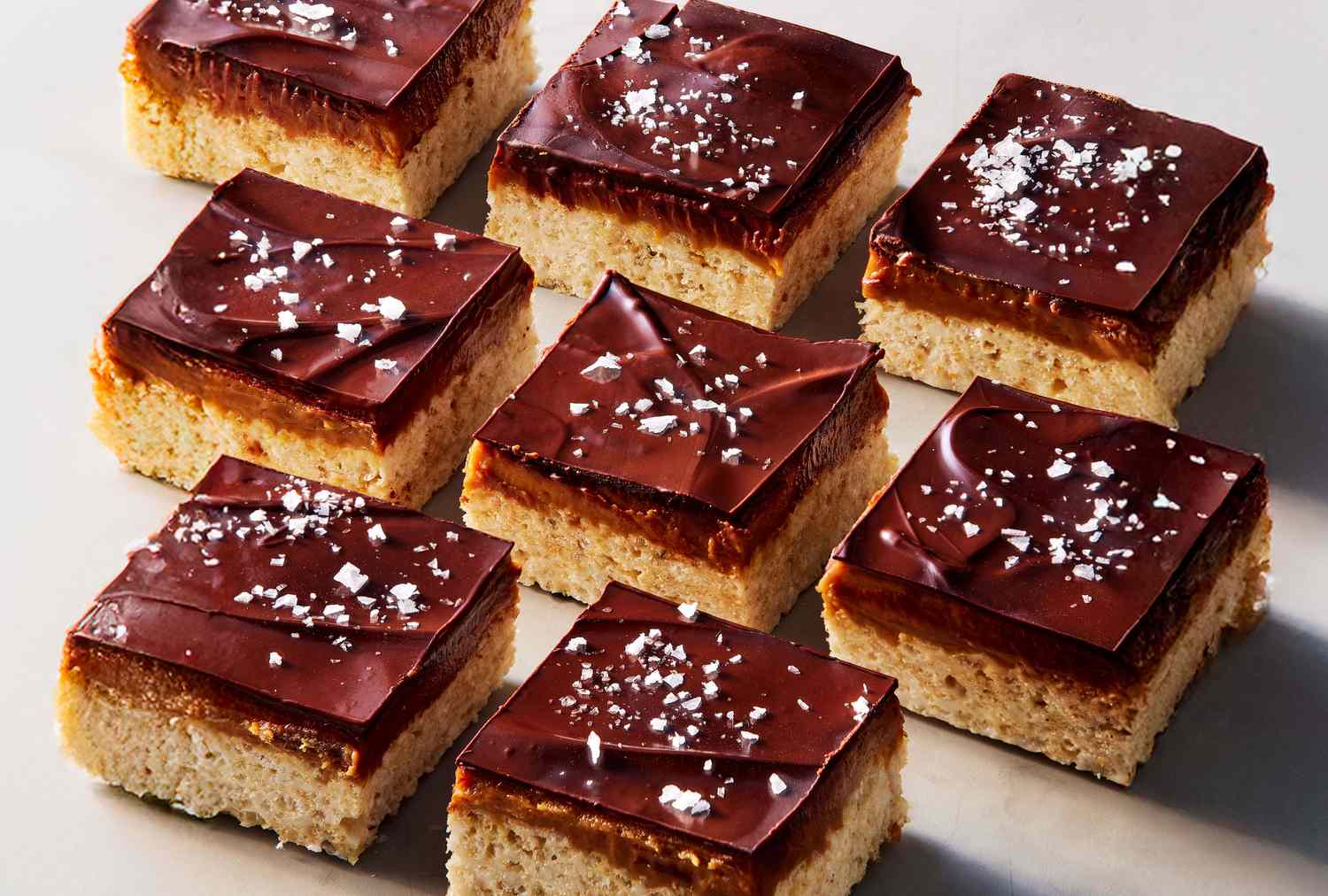 Chocolatetopped caramel cookie bars with a sprinkle of sea salt arranged in a grid format