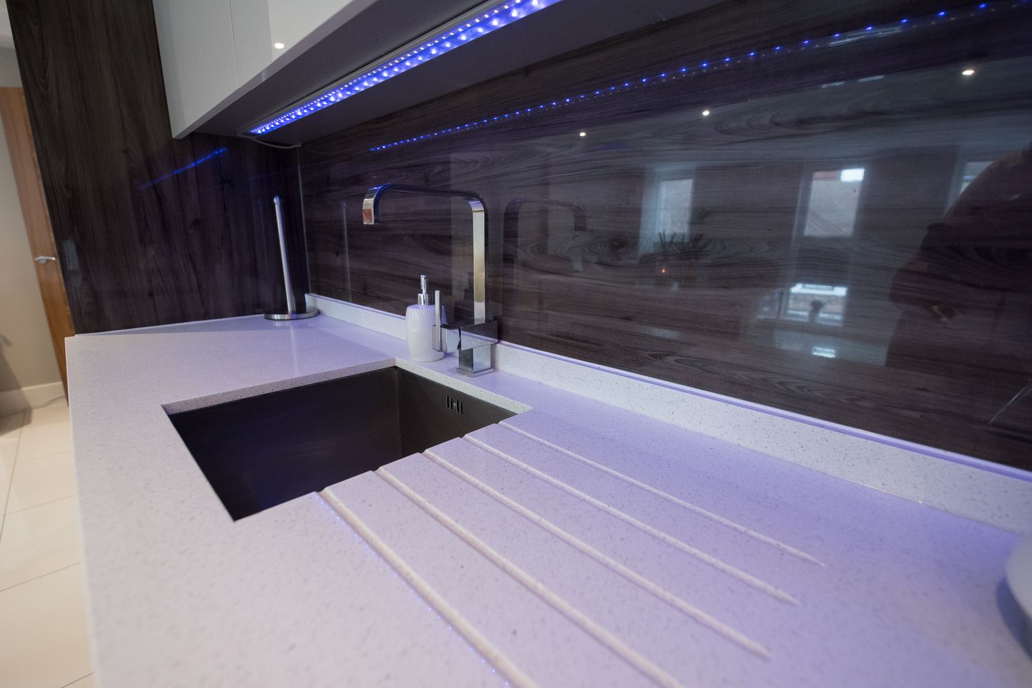 Modern kitchen sink with a glossy backsplash and countertop featuring a faucet and soap dispenser