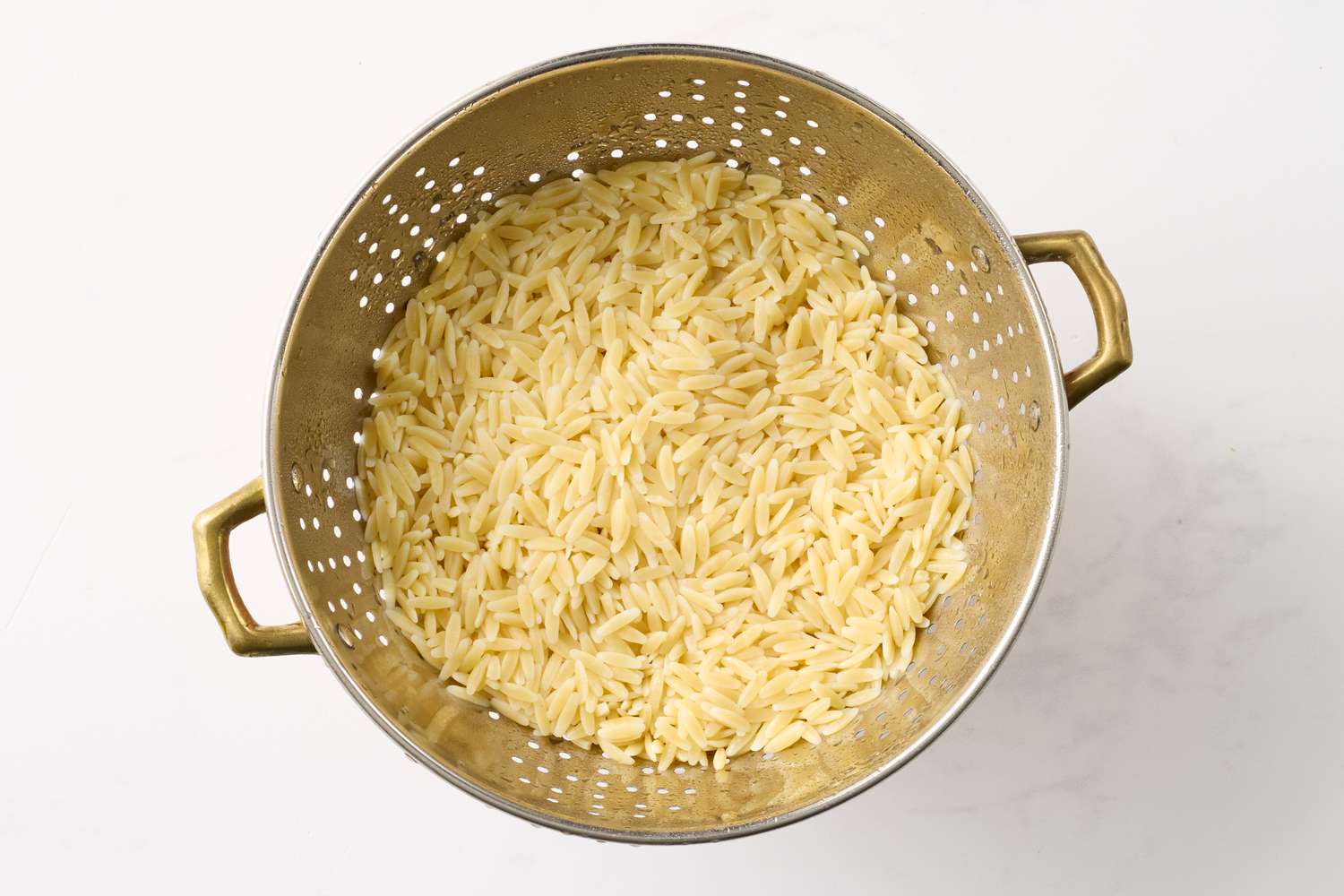 Drained cooked orzo pasta in a metal colander