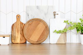 A collection of wooden and marble cutting boards arranged on a counter with potted plants nearby
