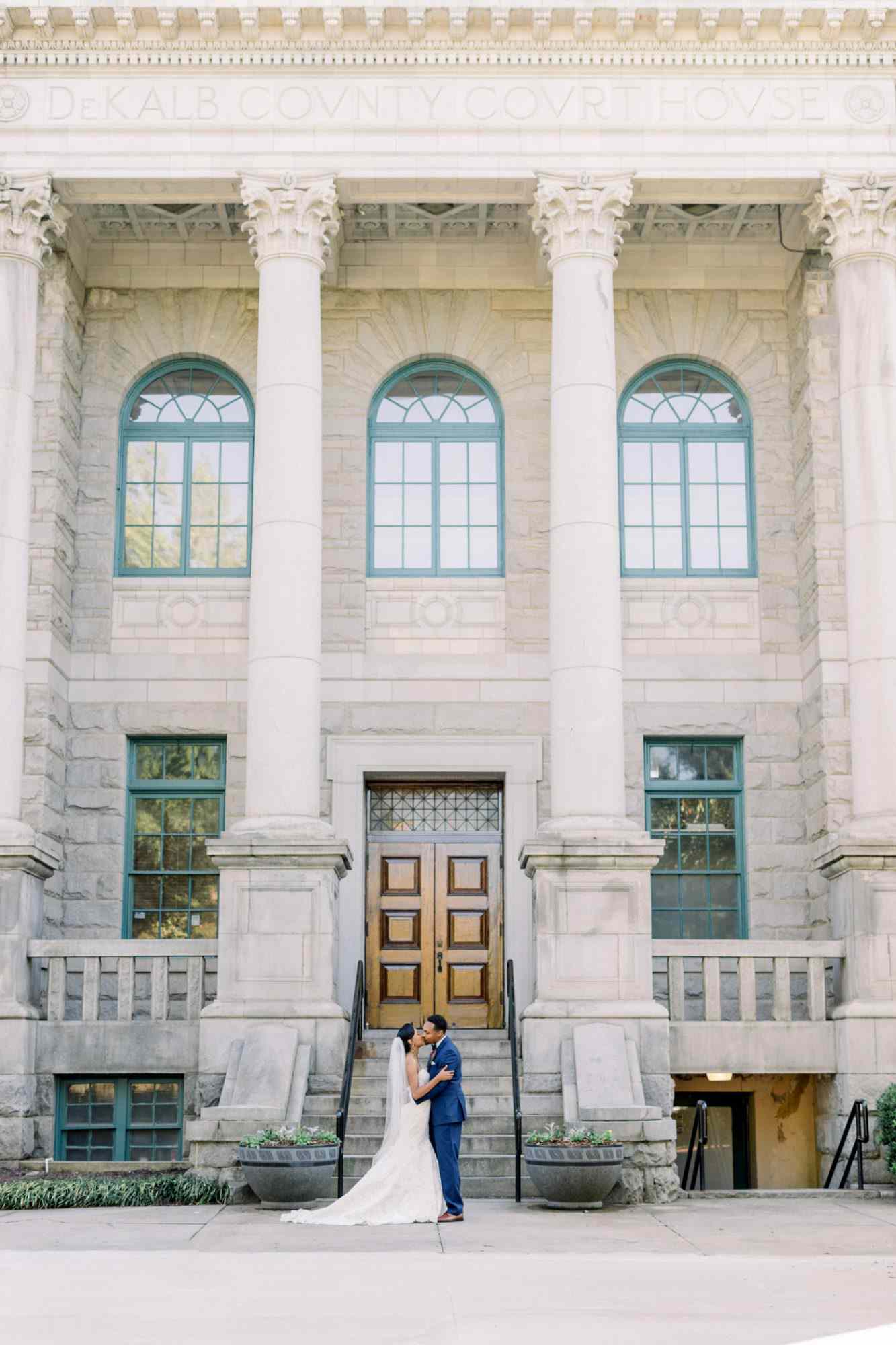 city hall wedding bride and groom kissing in front of building with arched windows and pillars