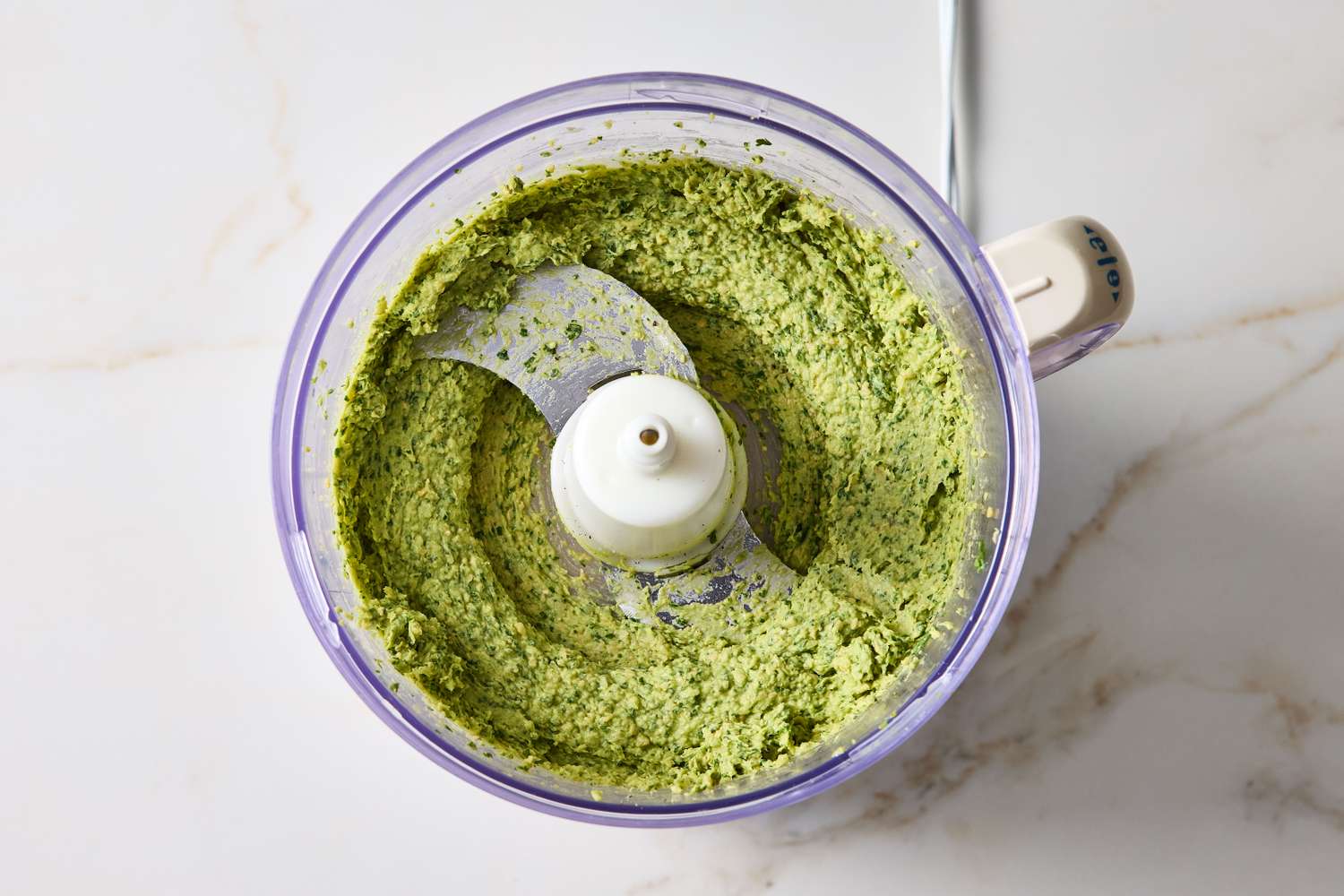 A food processor containing smooth blended guacamole hummus on a marble surface