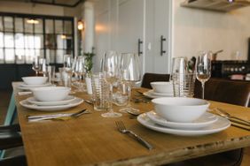 A dining table set with plates bowls glasses and cutlery in an indoor setting