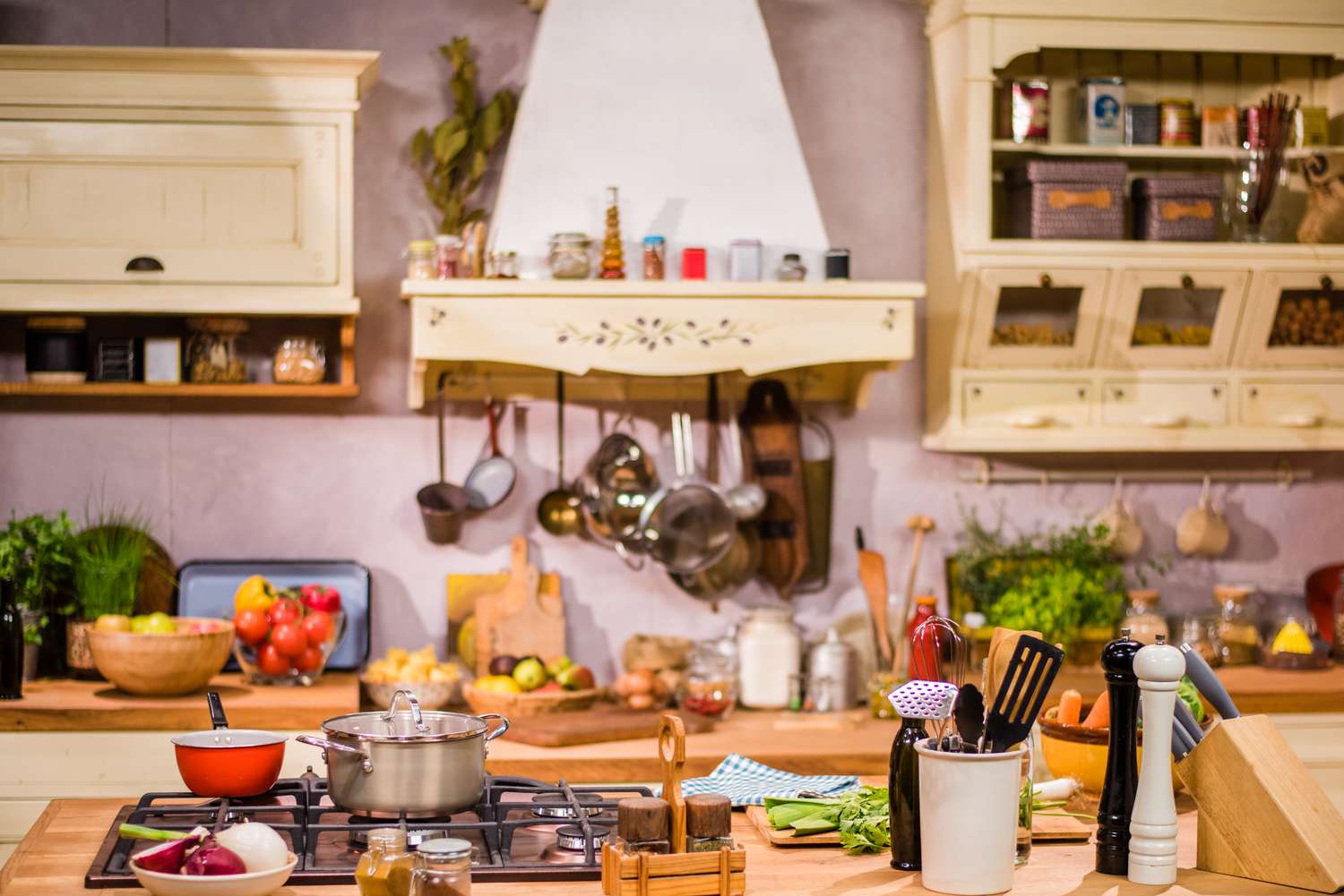 A kitchen counter with cooking utensils and ingredients displayed with shelves and a hooded stove in the background