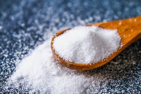 Crystals of shallow salt in a scoop, spoon on a dark gray table. Background for advertising salt.