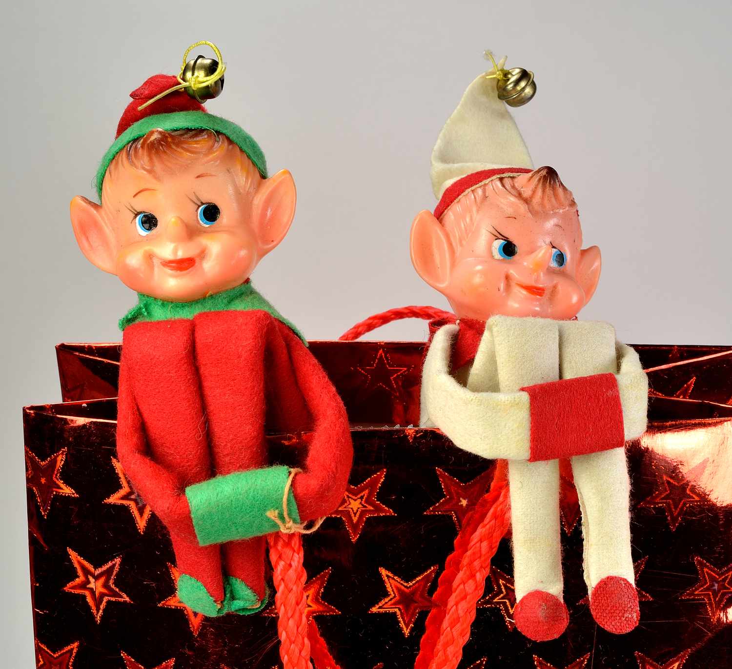 Two vintage elf figurines sitting on a festive gift bag
