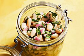 A jar filled with bean salad including white beans chopped herbs and diced red onions