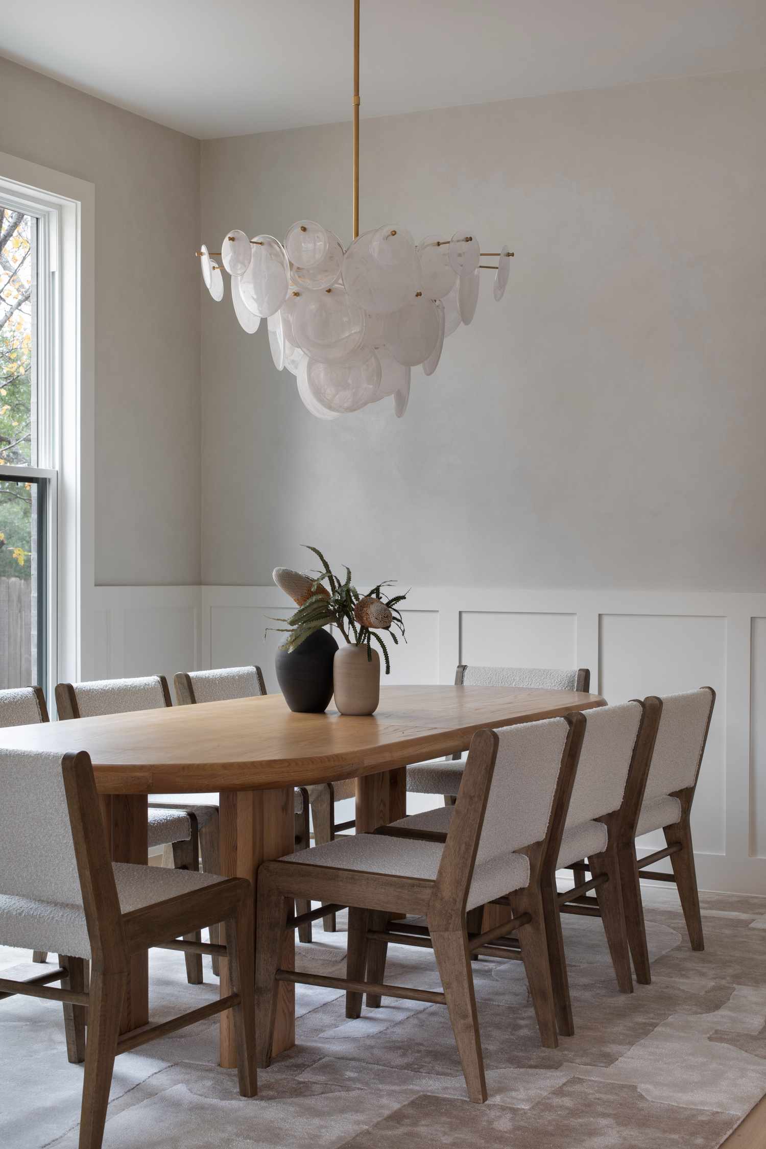 A dining room featuring a wooden table chairs a modern chandelier and decorative vases