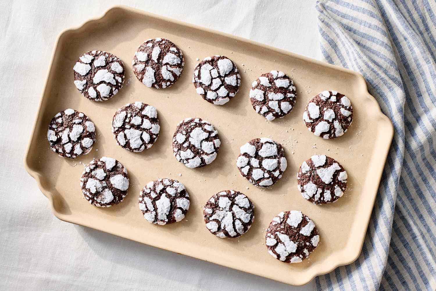 A tray of chocolate crackle cookies with powdered sugar coating placed on a lightcolored surface