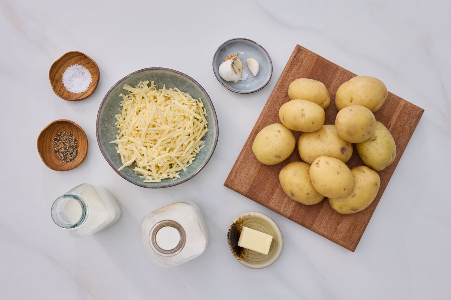 Ingredients for scalloped potatoes arranged on a counter including potatoes grated cheese butter cream salt and garlic