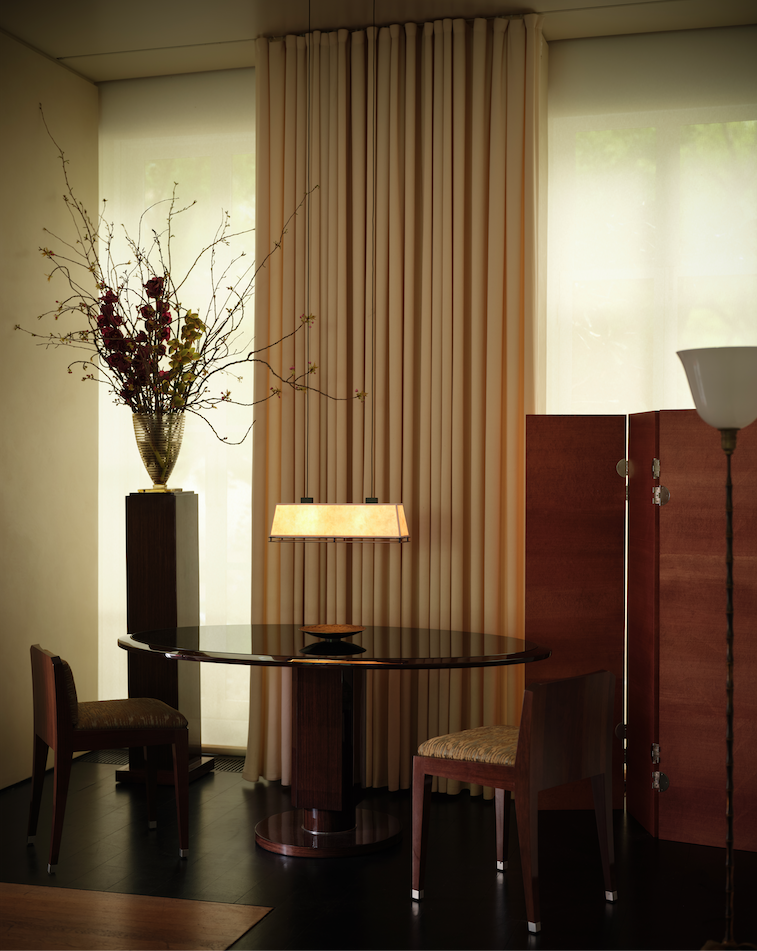 A luxurious interior with a table two chairs a lamp decorative flowers and tall curtains
