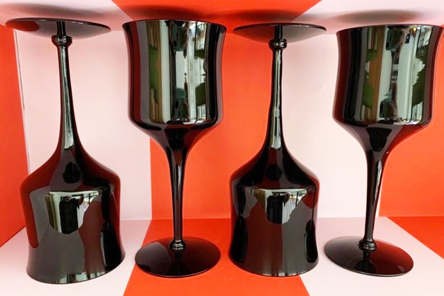Four black goblets with reflective surfaces placed on a red and white background two are upside down and two are upright