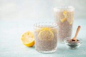 Two glasses of chia seed water with lemon slices, a lemon half, and a bowl of chia seeds with a spoon on the side