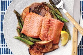 Cooked salmon served on a plate with asparagus mushrooms and a lemon wedge