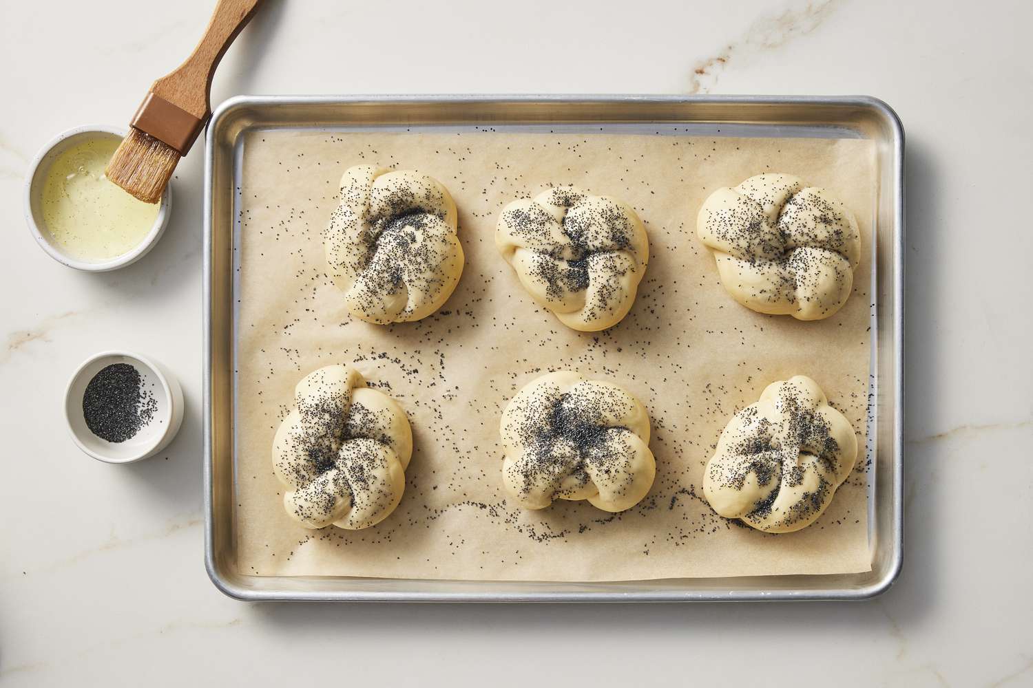 Knotted dough on baking sheet with poppy seeds and butter