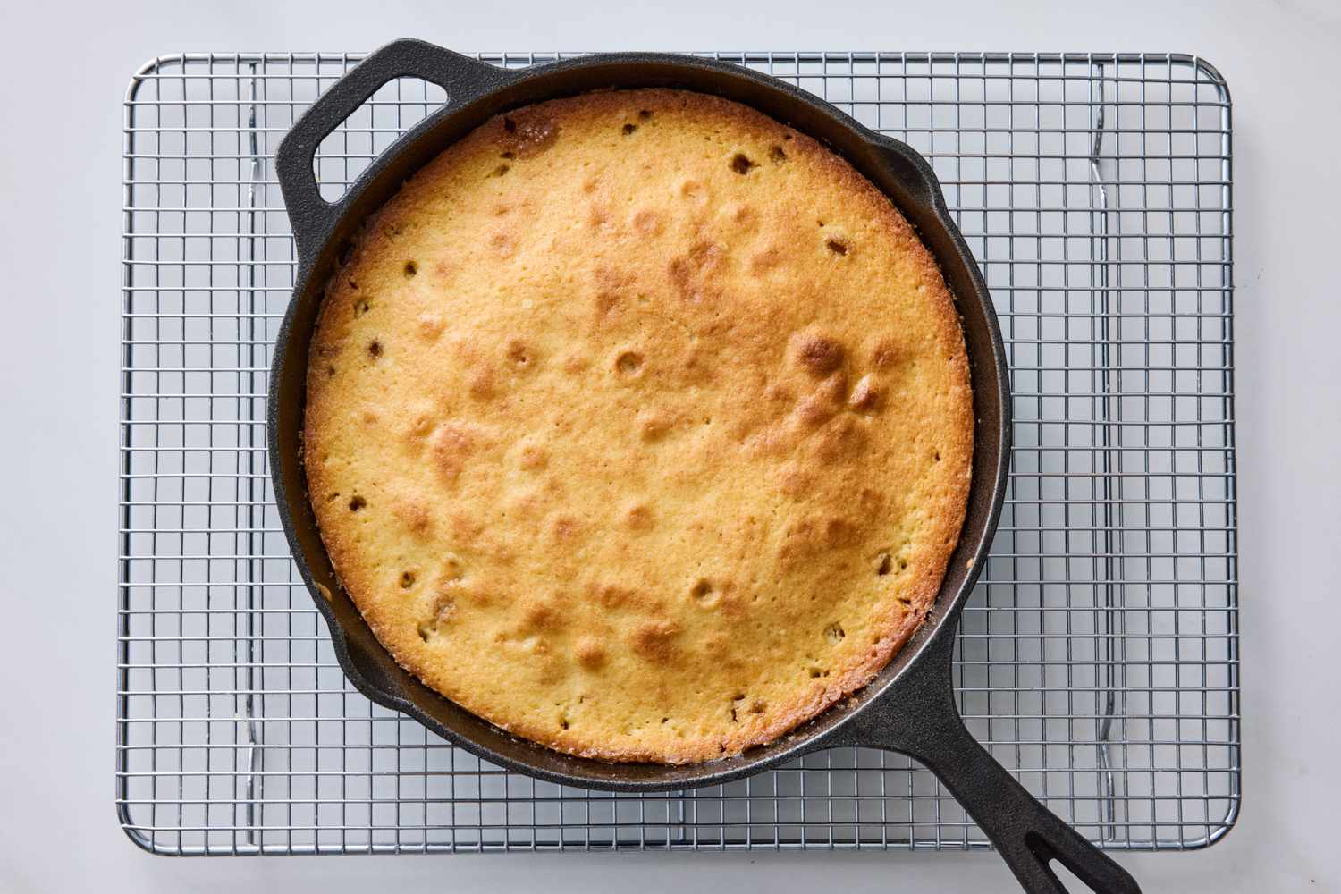 Pear upsidedown cake in a cast iron skillet cooling on a wire rack