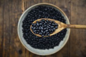 Wooden spoon holding black beans over a bowl filled with black beans