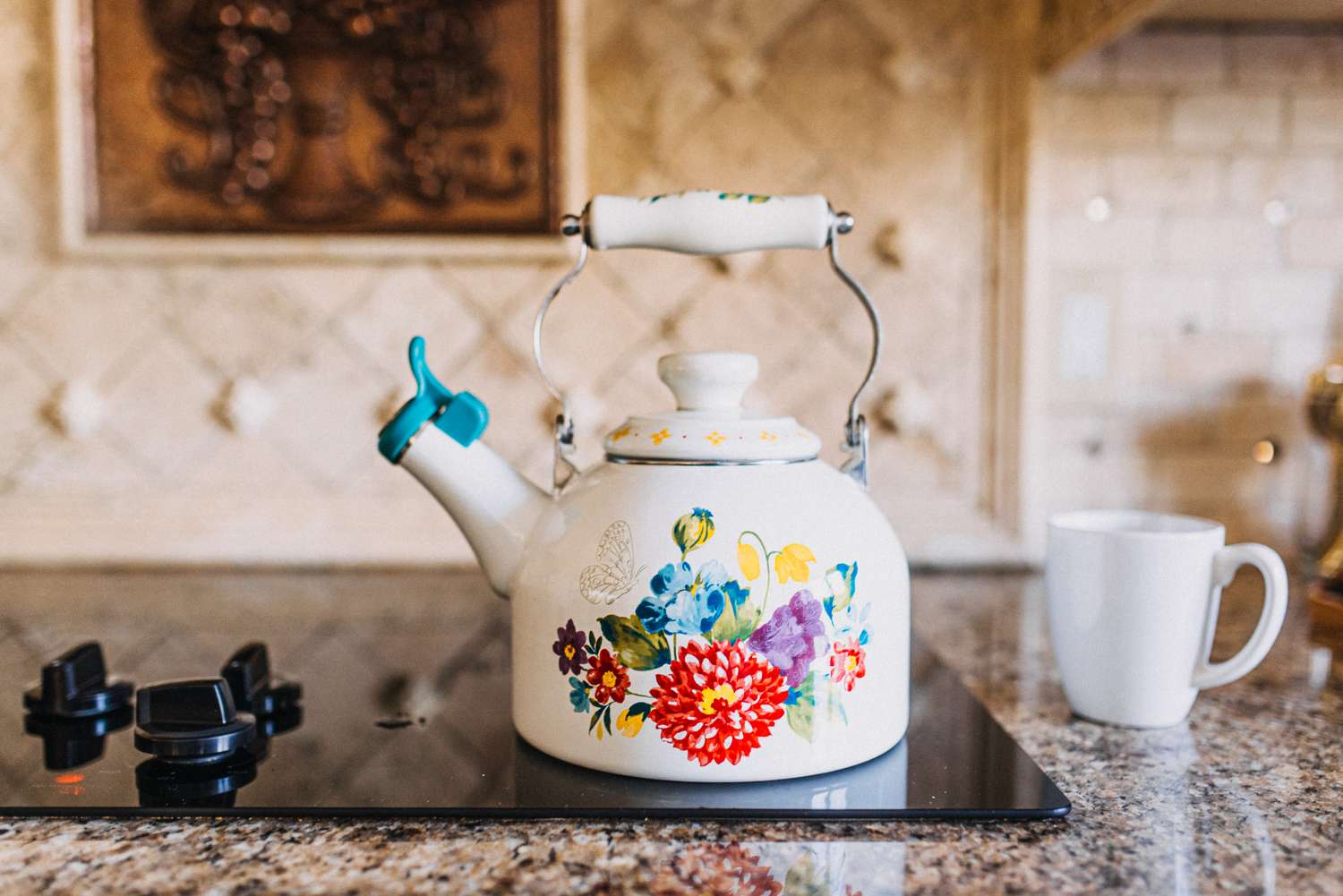 A floralpatterned teapot on a kitchen stovetop next to a white mug