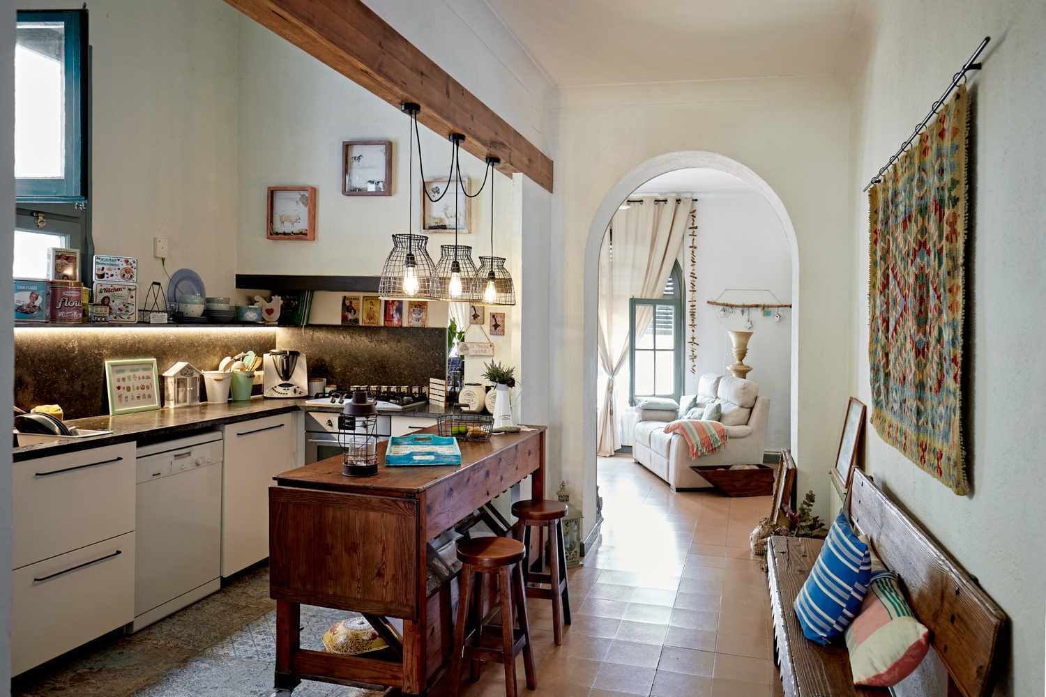 A cozy kitchen and dining area with a wooden island and stools opening into a sitting room through a rounded archway