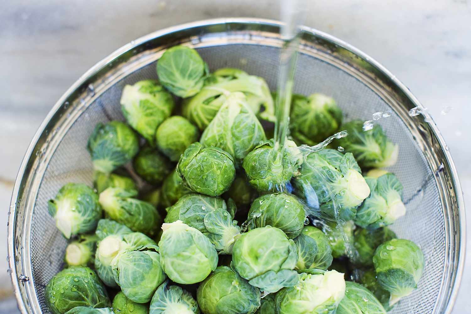 Brussels sprouts being rinsed with water in a metal colander