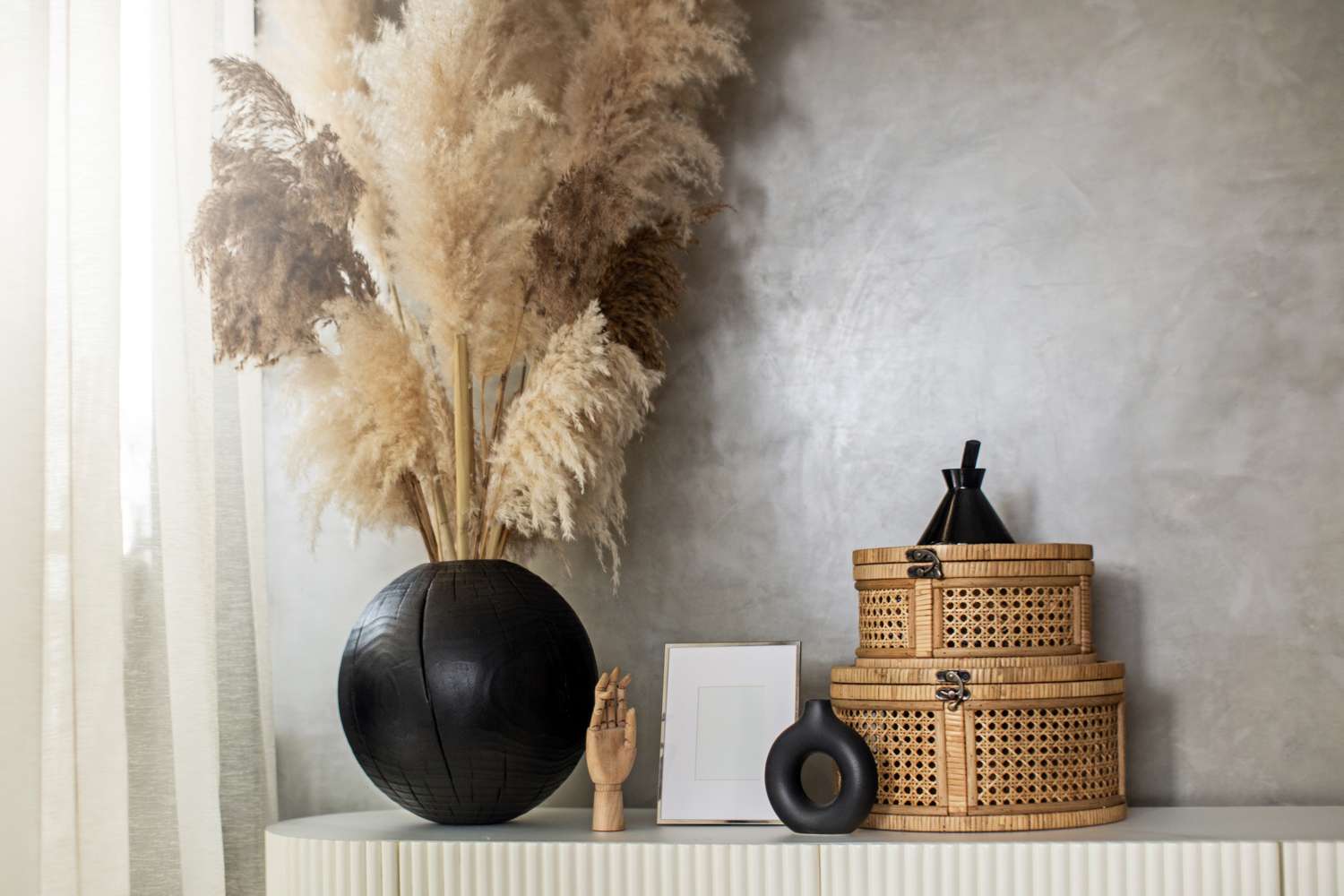 A decorative arrangement with a vase of pampas grass stacked wicker baskets and small sculptures on a lightcolored surface