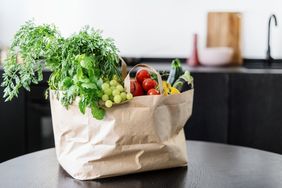 A grocery bag on a table containing fresh vegetables and fruits