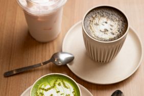 Two ceramic cups of drinks one a matcha beverage and the other a latte placed on saucers on a wooden table with spoons