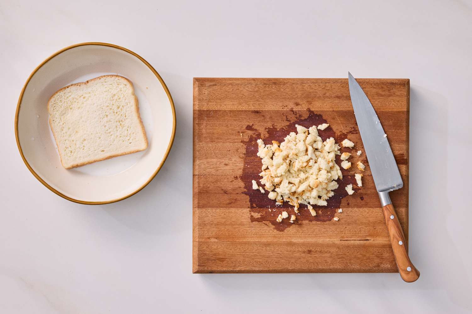 A cutting board with a knife and chopped ingredients next to a plate with a slice of bread