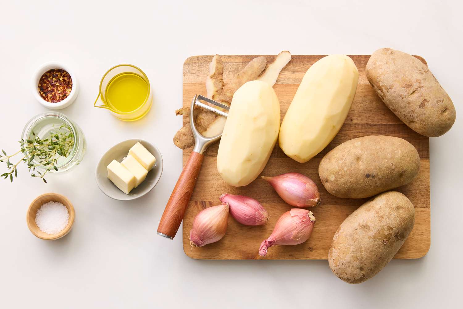 Ingredients for a crispy potato roast including potatoes shallots butter thyme oil and a seasoning blend arranged on a cutting board