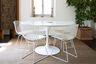 Round white table with wire chairs indoor setting with a carpeted floor and decorative backdrop