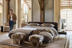 A man stands in an upscale bedroom with a large bed and furcovered stools