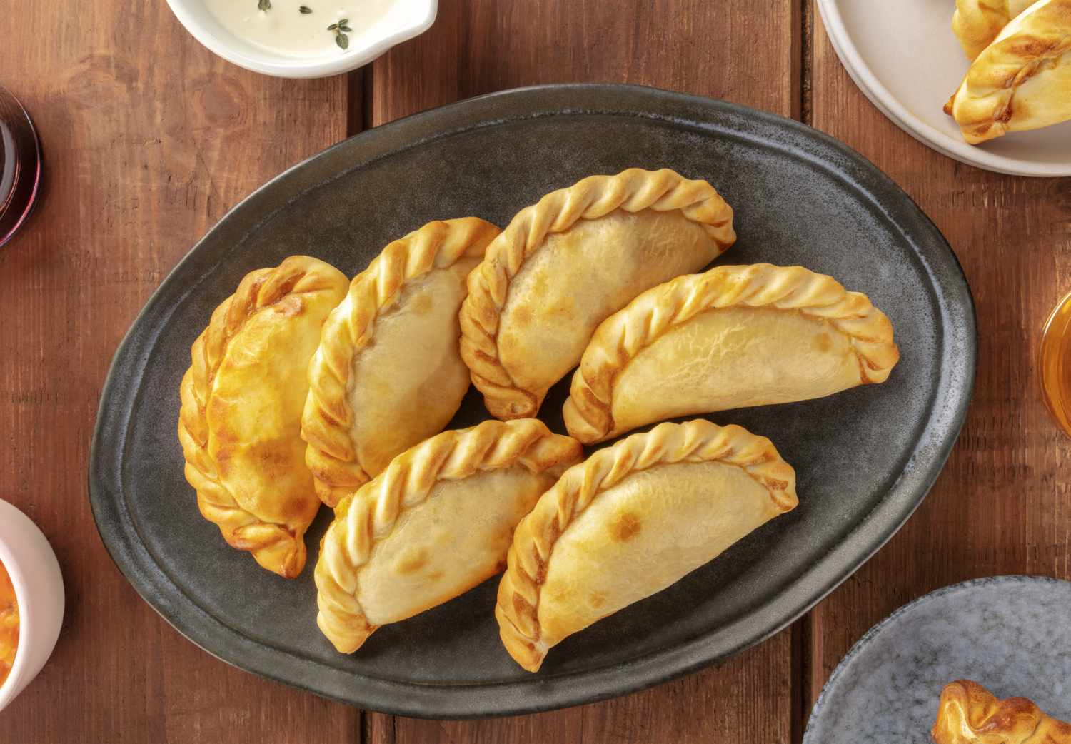 A serving plate with six empanadas placed on a table, side dishes partially visible around