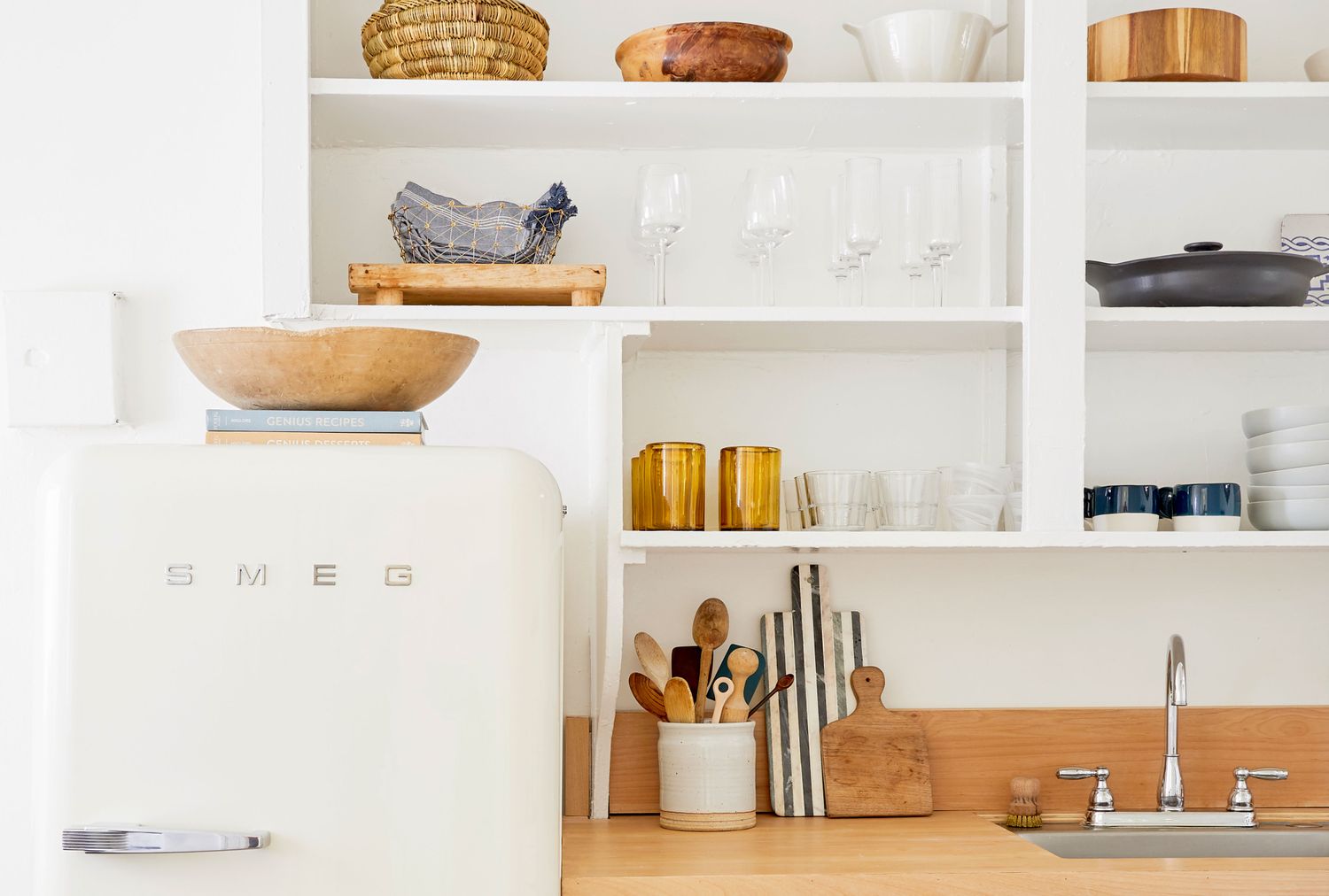 Kitchen countertop with SMEG refrigerator open shelves displaying glassware and dishes and a sink faucet on the right side