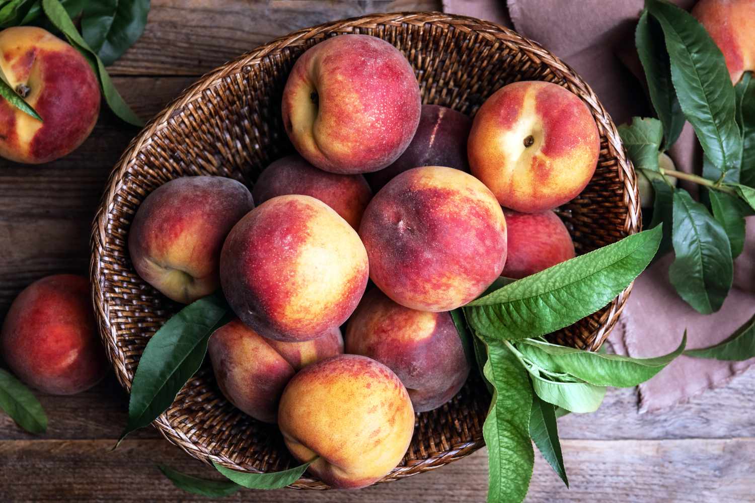 A basket filled with peaches and leaves on a wooden table
