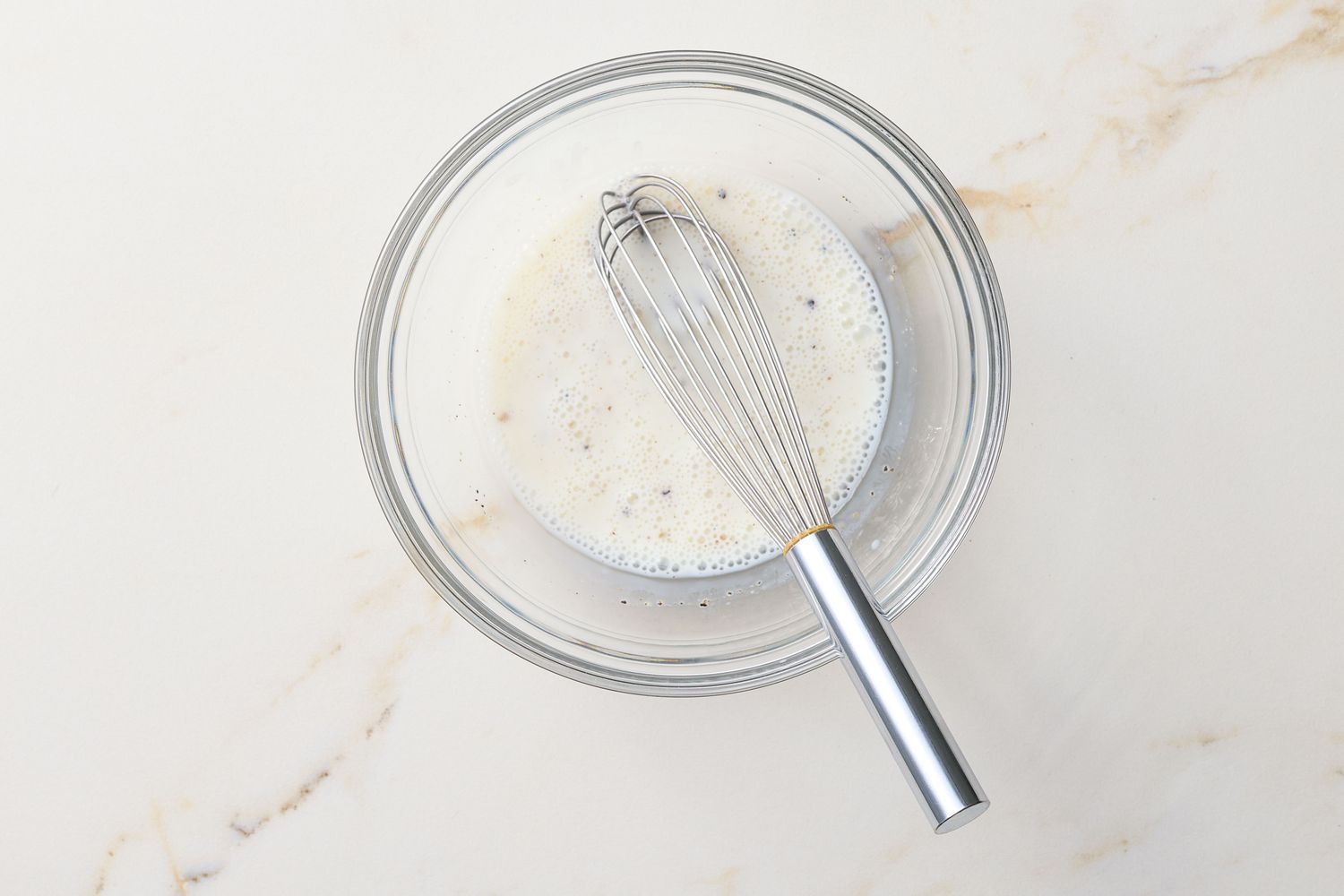 A whisk in a bowl containing a creamy mixture, likely preparation of buttermilk herb vinaigrette