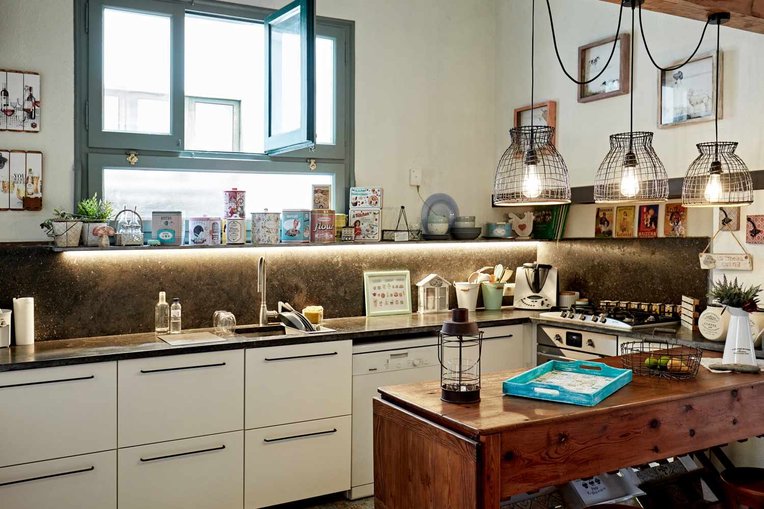 A kitchen interior with a countertop sink cabinets and an island table under hanging lights featuring various decorations