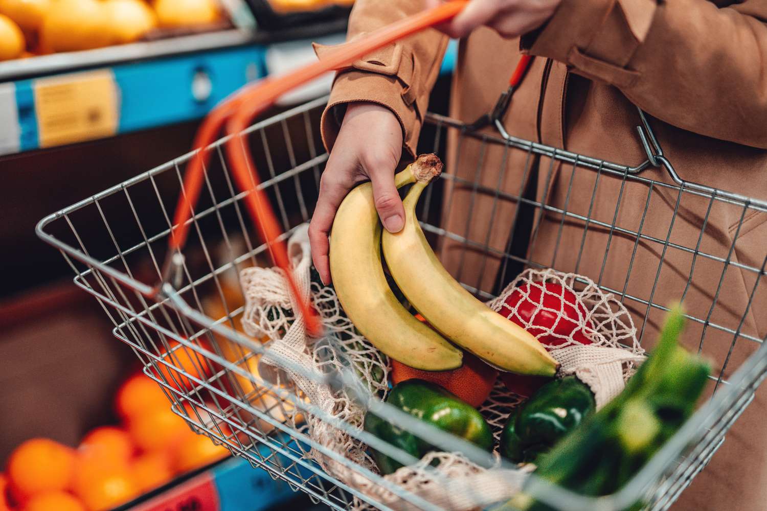 Person carrying a shopping basket containing bananas and other fruits and vegetables