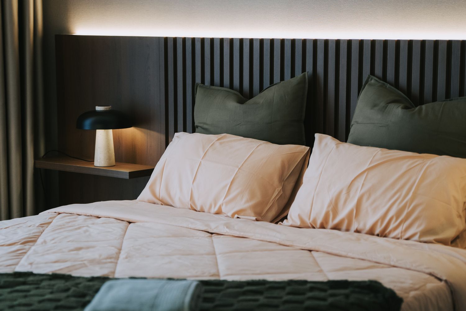 A bedroom setup with a bed pillows a nightstand and a lamp