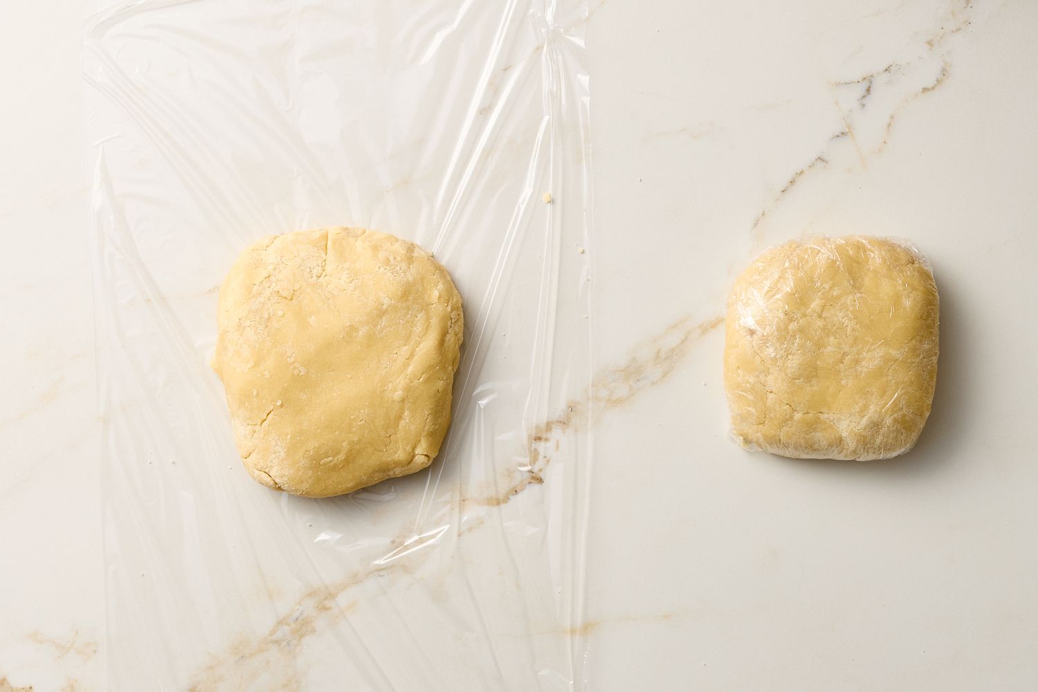 Two portions of cookie dough one wrapped in plastic and one unwrapped on a marble surface