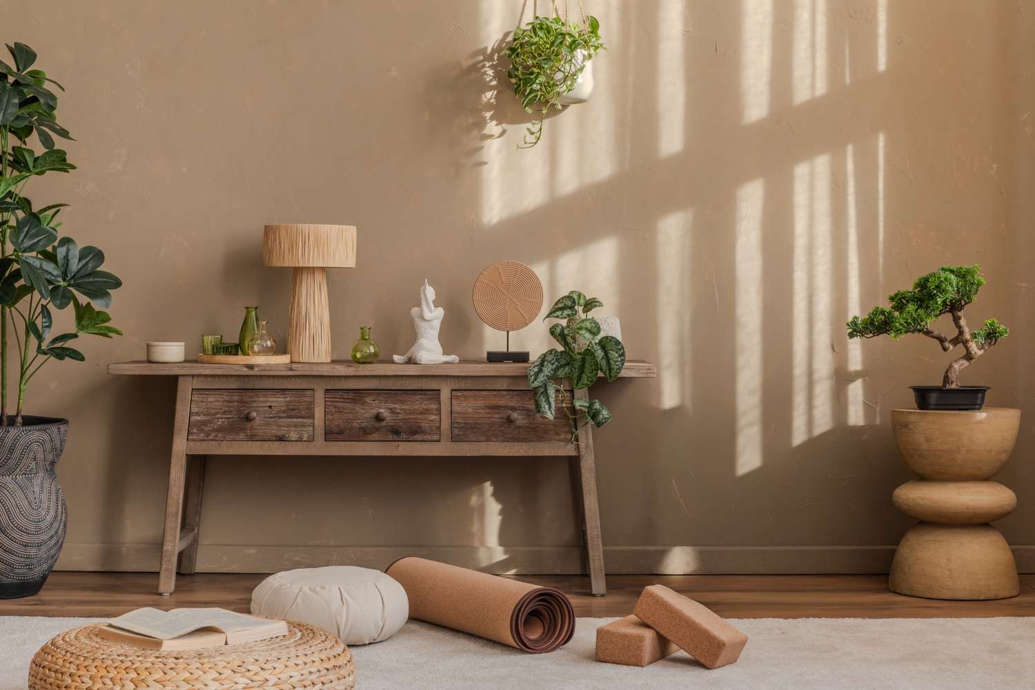 A meditation space with a wooden console table a yoga mat cushions potted plants and a small statue on the table