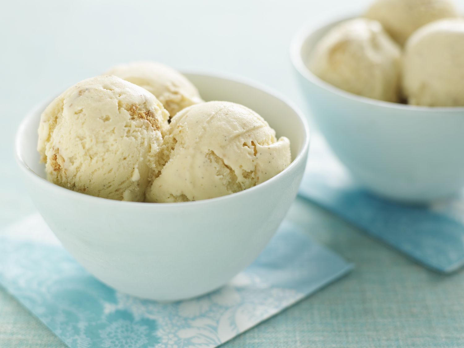 Two bowls filled with scoops of ice cream placed on bluepatterned napkins