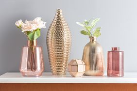 A set of decorative vases and containers some with flowers or greenery arranged on a white shelf