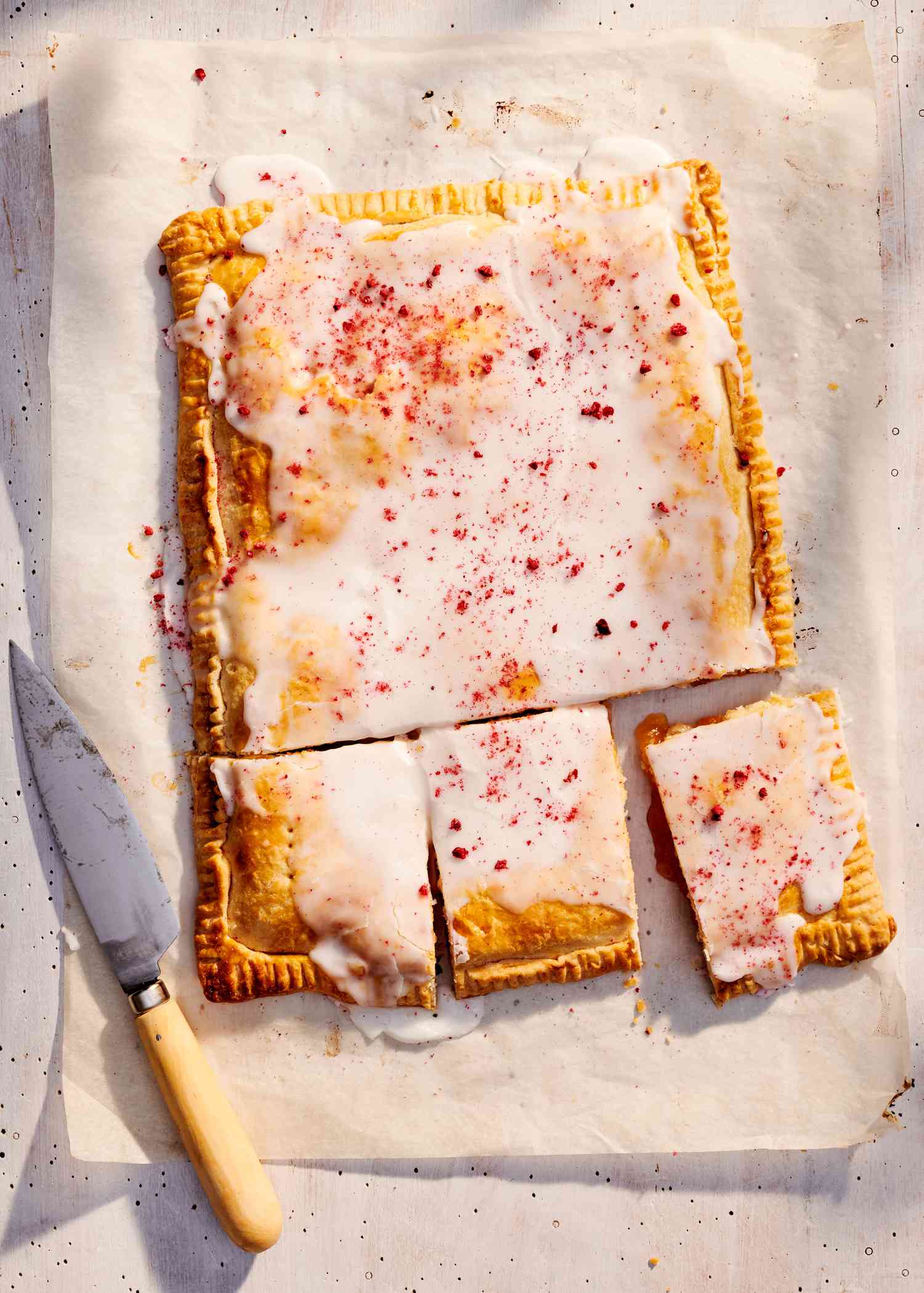 Iced pastry with knife on parchment